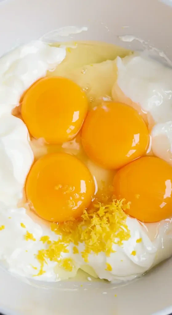 Jaunes d'œufs, yaourt grec et zeste de citron dans un bol, prêts à être mélangés pour obtenir une texture homogène et préparer le Gâteau Nuage au Yaourt