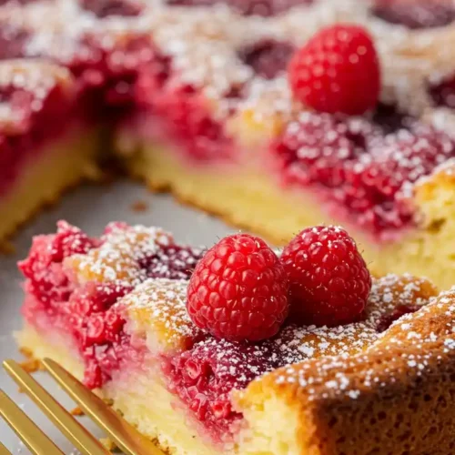 Présentation d'une portion de Clafoutis Aux Framboises, un dessert français traditionnel, avec des framboises juteuses éclatant sur une pâte délicate, saupoudrée de sucre glace et prête à être dégustée avec une élégante fourchette dorée.