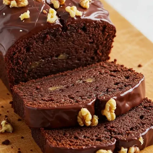 Un pain de gâteau aux bananes et chocolat tranché, décoré d'un glaçage au chocolat et de noix concassées, sur une planche à découper.