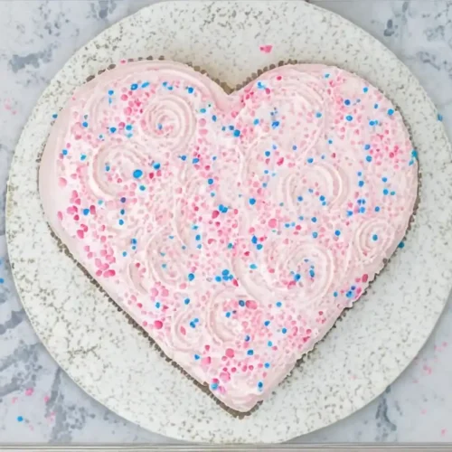 Vue de dessus d'un gâteau Saint-Valentin en forme de cœur, recouvert d'un glaçage rose et de décorations colorées.