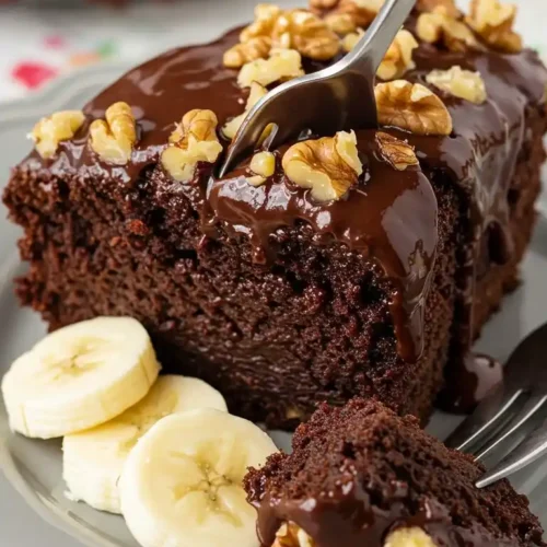 Une part de gâteau aux bananes et chocolat, nappée de glaçage et de noix, servie avec des rondelles de bananes fraîches.